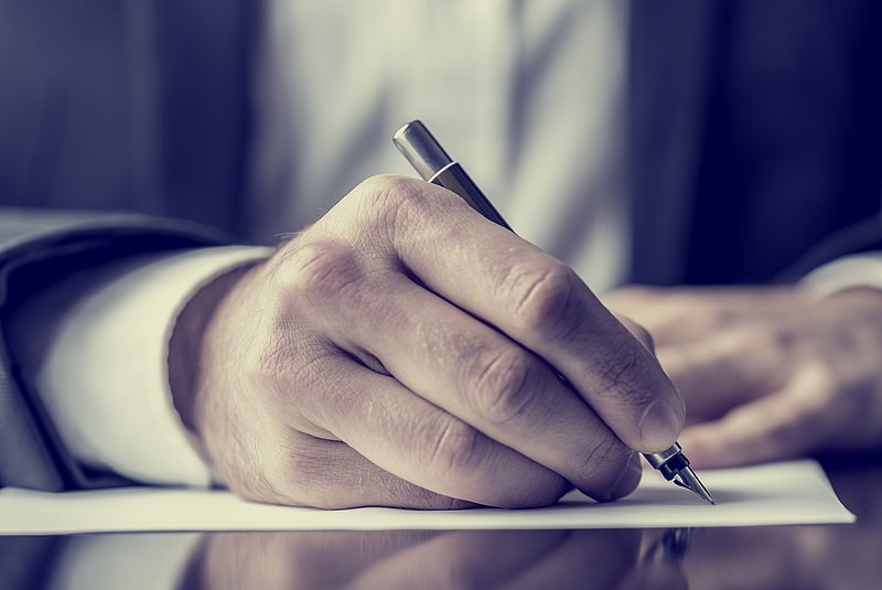 Männliche Hand hält einen Stift und schreibt auf einem Blatt Papier auf einem Tisch