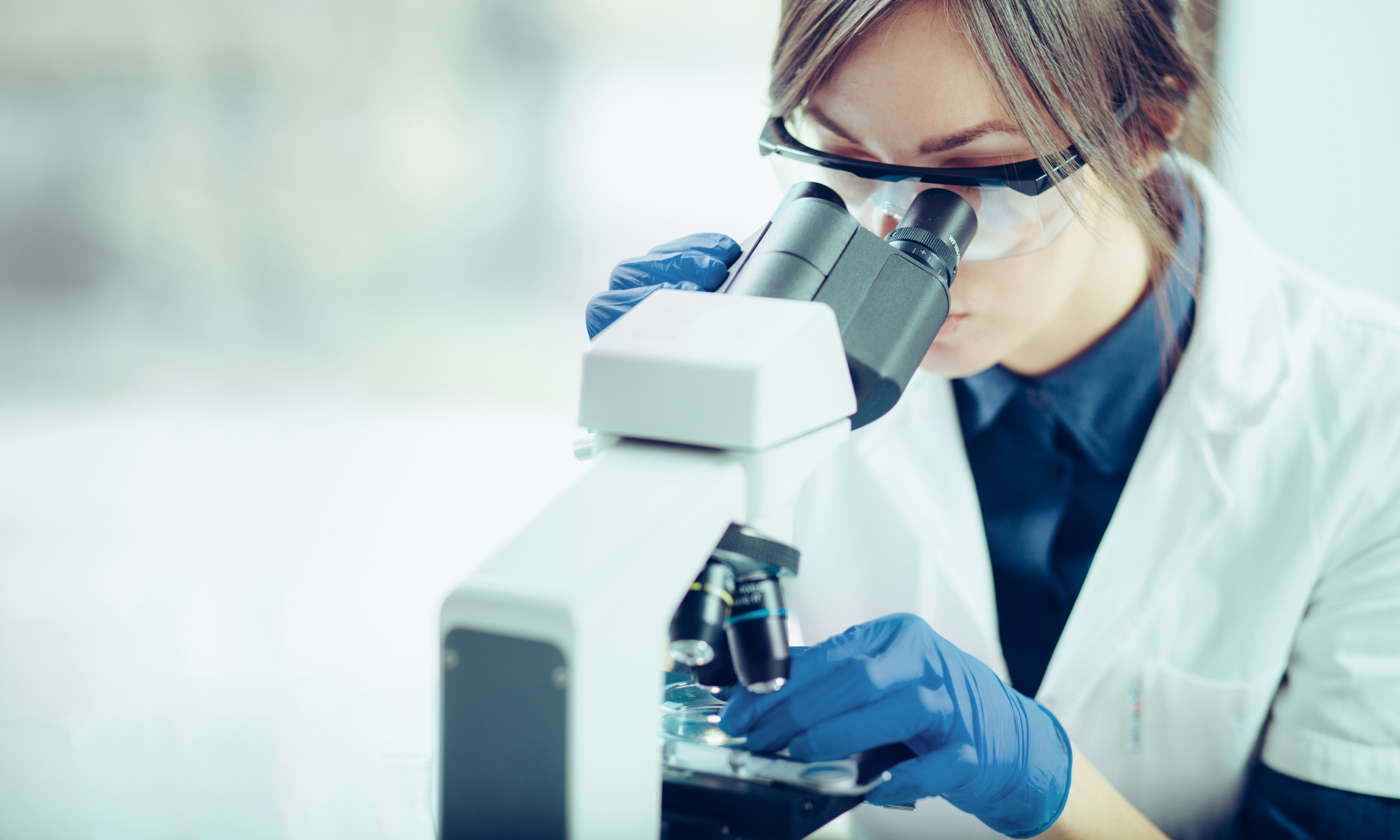 In einem Labor schaut eine Wissenschaftlerin durch ein Mikroskop durch